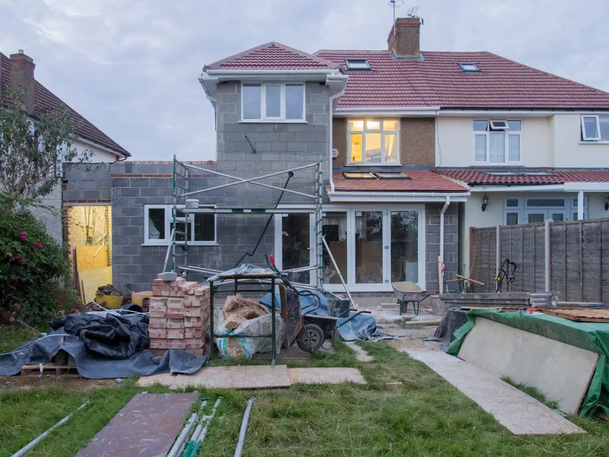 A semi-detached house from the garden, a single-storey blockwork extension built across the back with scaffolding and pallets of bricks
