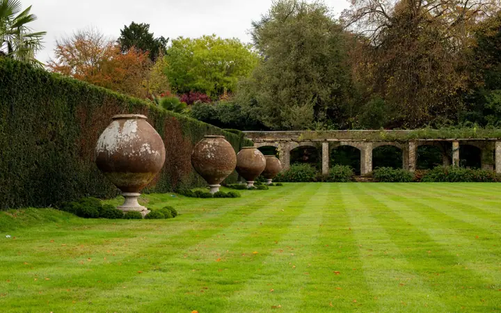 A wide striped lawn edged by stone urns and a clipped hedge