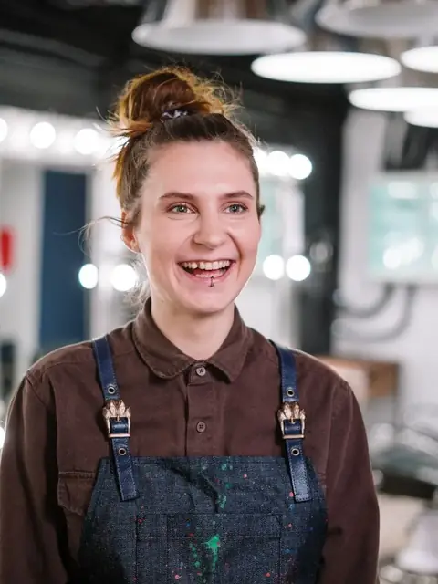 Mia, senior stylist, laughing warmly in her work apron on the salon floor