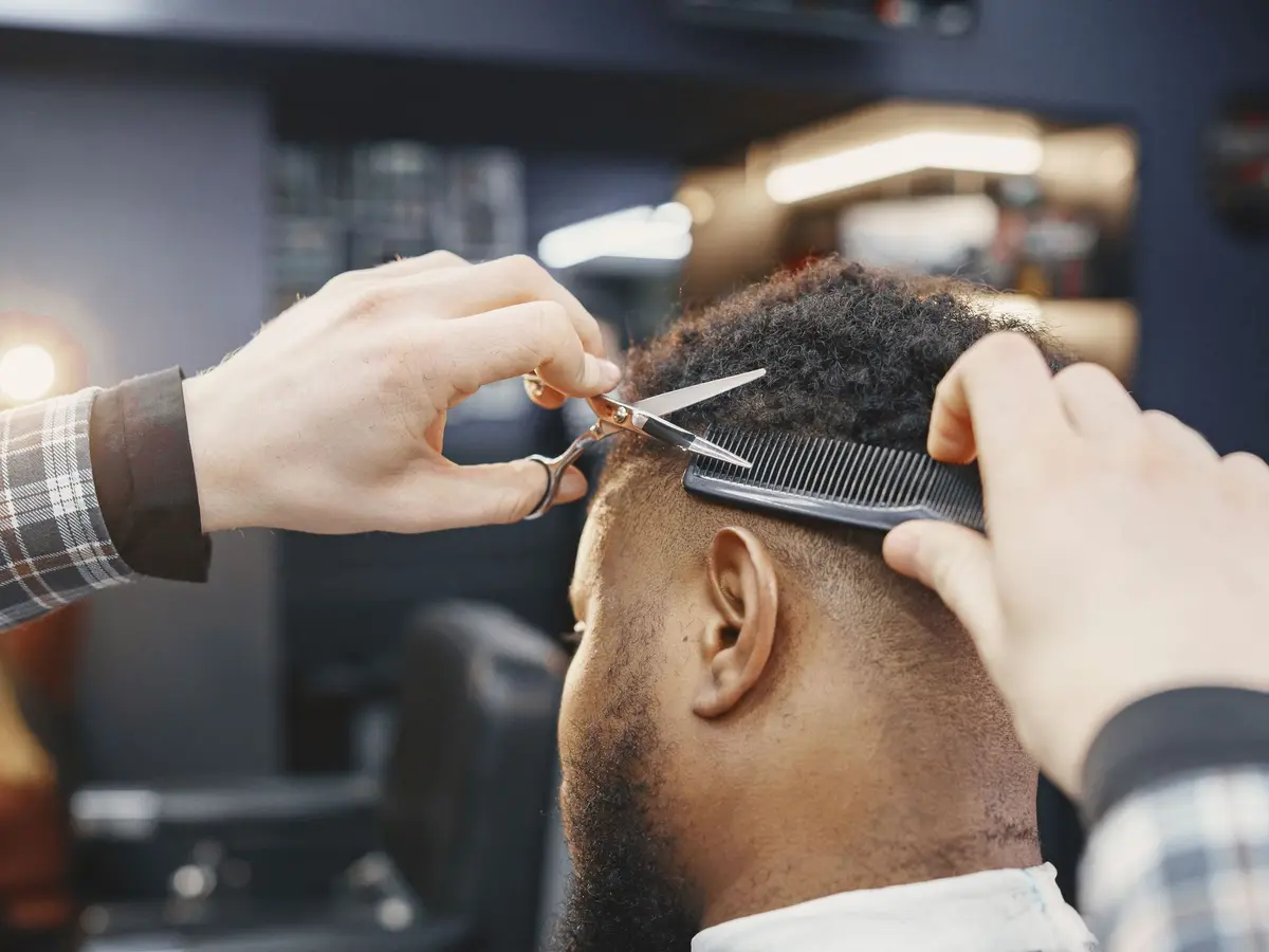 A barber cutting a client's hair with scissors over a comb