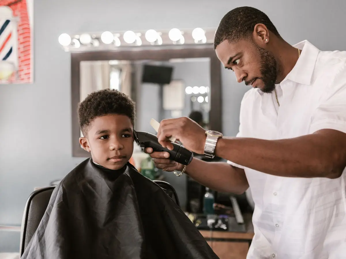 A young boy in a cape sitting calmly while a barber cuts his hair with clippers