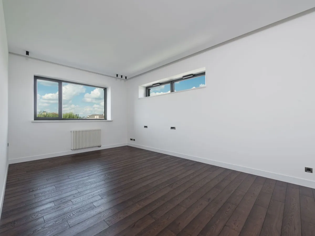 A clean, empty room with fresh white walls, a dark wooden floor and two windows
